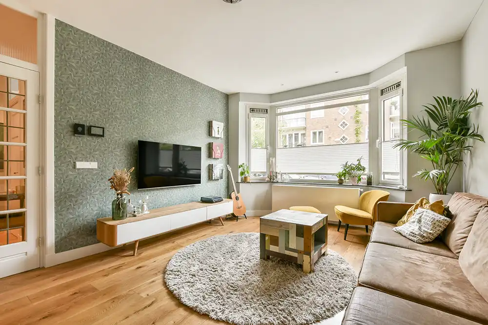 Ein stilvolles, modernes Wohnzimmer mit einem bequemen Sofa, einem dekorativen Teppich und großen Fenstern, die Tageslicht hereinlassen. 